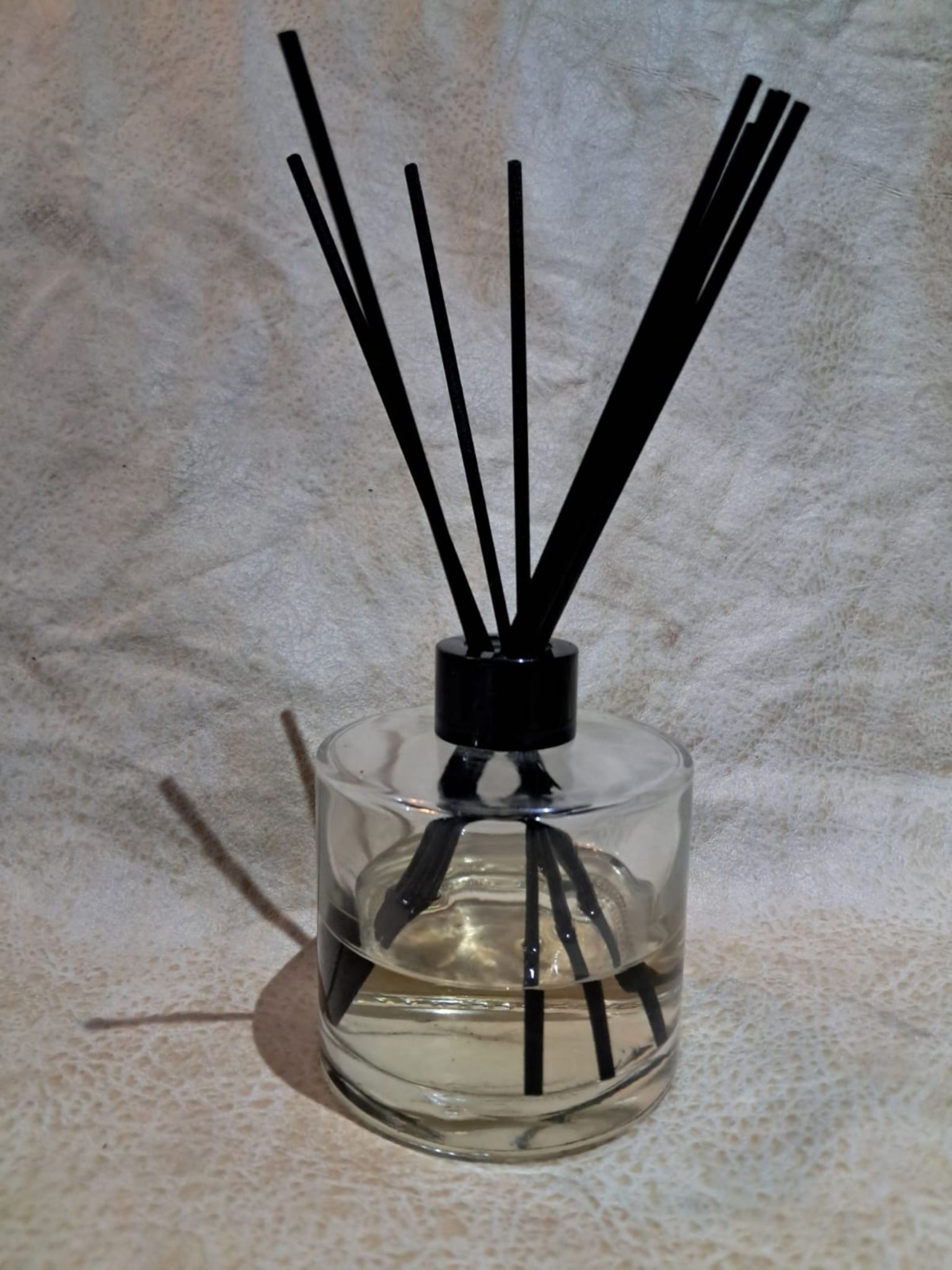 A clear glass diffuser bottle filled with a light-colored liquid, topped with a black cap.